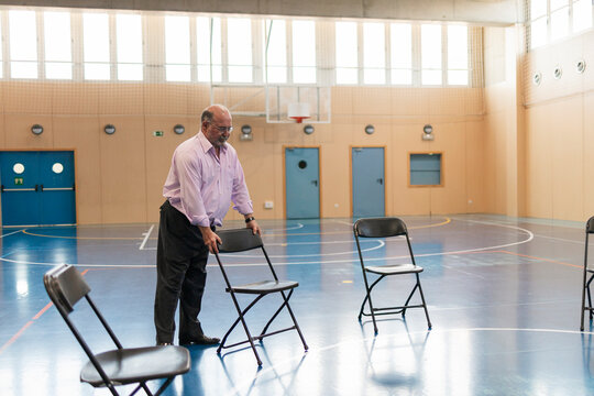 Senior man arranging chairs in empty gym