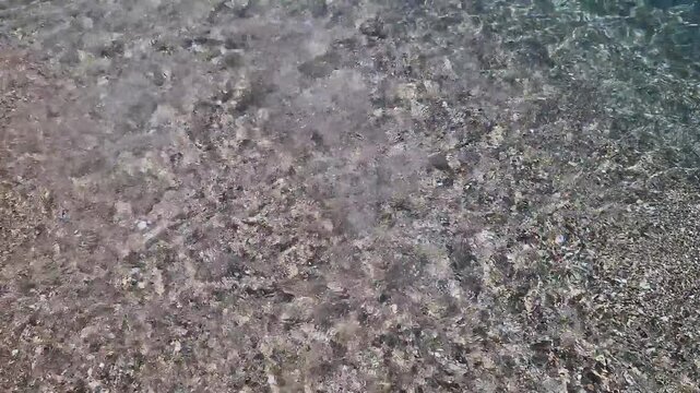 Sea wave rushes onto the sandy shore of the beach. Close-up of sea water on the coast on a sunny day. Summer seascape with surf line and clear water. Black Sea, Bulgaria. Resort vacation concept