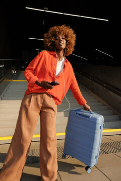 Woman travels with smartphone, earphones and suitcase