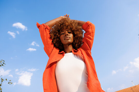 Woman raises arms beneath blue summer sky