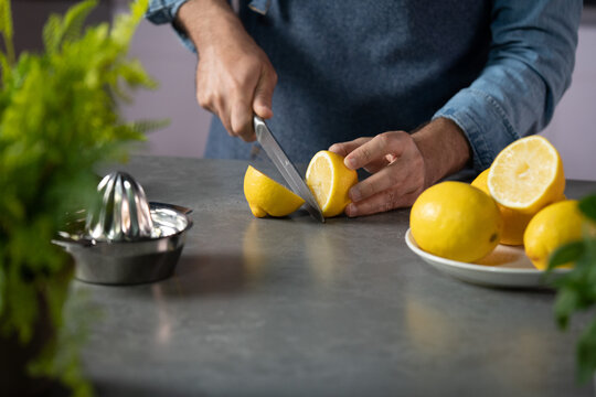 Man slicing fresh lemon for juice in kitchen