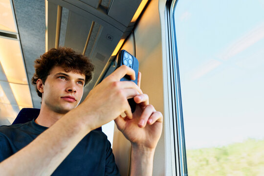Young Man Takes a Photo on a Train While Looking out the Window