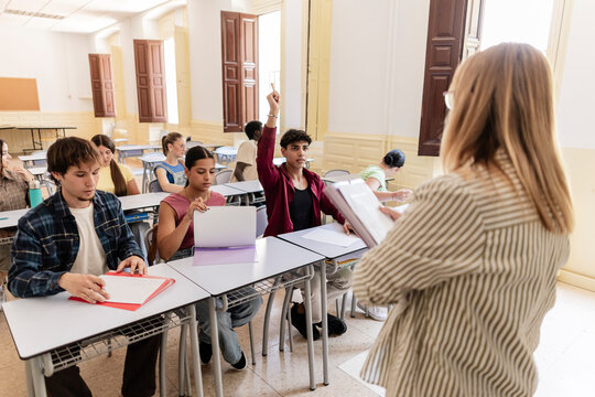 Students raising hand answering questions during classroom lesson