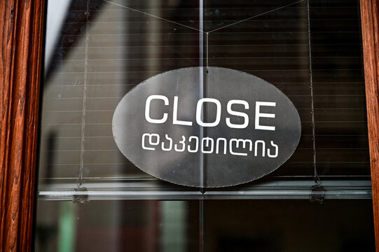 Oval sign with the word "Close" and the Georgian text "daketilia" on a glass door, indicating the closing of a shop or restaurant for the day or a day off; close-up shot in Tbilisi, Georgia.
