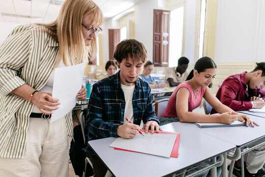 Teacher assisting young student during exam in classroom