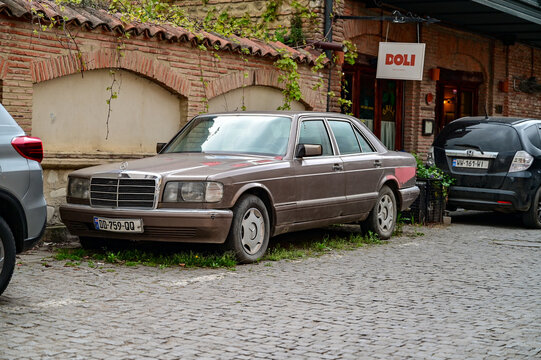 Brown Mercedes-Benz W126 S-Class classic car from the 1980s parked on cobblestones in front of a historic brick wall in Telavi, classic German luxury car, Kakheti, Georgia 11.04.2025