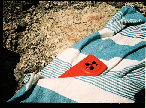 Red smartphone on striped towel at rocky beach