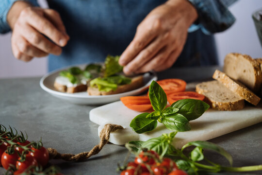 Person preparing healthy avocado toast with fresh basil