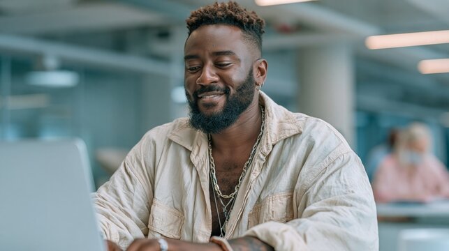 Smiling black businessman enjoying work on his laptop in a contemporary office setting