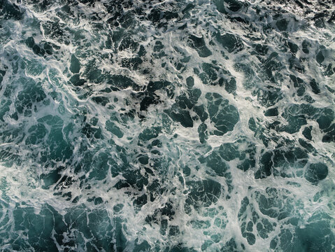 Foaming waves form an energetic abstract pattern across dark water in the North Sea, UK