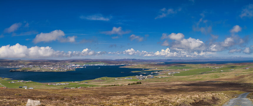 Wide coastal view of Lerwick Bressay and Viking Wind Farm in Shetland UK beneath dramatic blue skies
