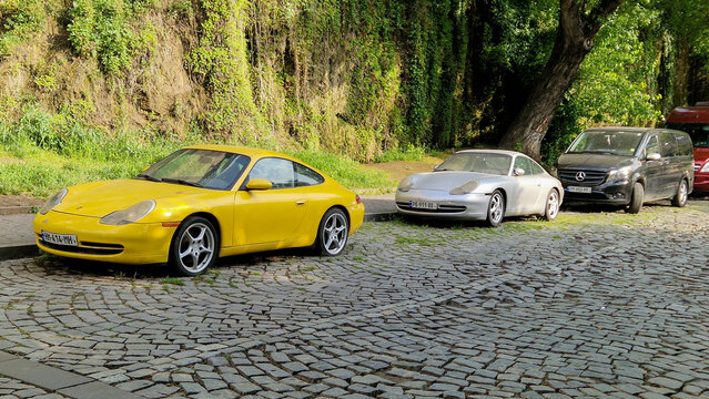 Two yellow and silver Porsche 911 Carrera Coup&eacute;s (996 series) parked on cobblestones in Tbilisi; classic German sports cars, capital region, Georgia 15.4.25