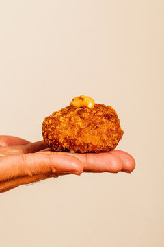 Hand holding a crispy golden croquette topped with orange sauce