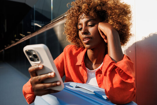Woman checking smartphone beside blue suitcase outdoors
