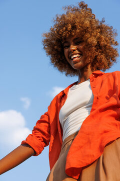 Smiling woman wearing orange overshirt under blue sky