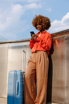 Woman using smartphone beside suitcase during travel