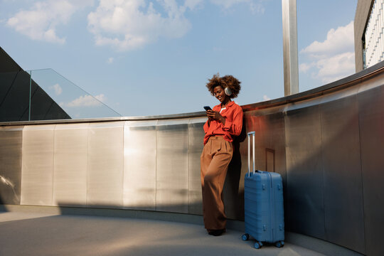 Woman using smartphone beside blue suitcase