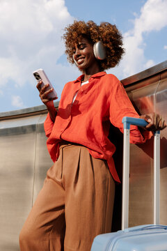 Woman with orange shirt using smartphone and suitcase