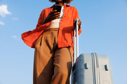 Woman with smartphone and suitcase under blue sky