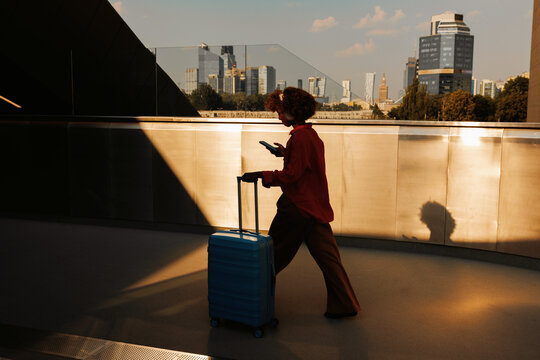 Woman checks smartphone while pulling suitcase in city