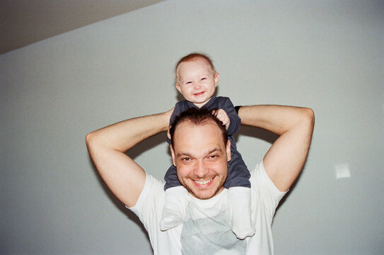 Man lifts baby on shoulders while smiling