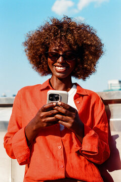 Woman using phone wearing orange shirt under blue sky