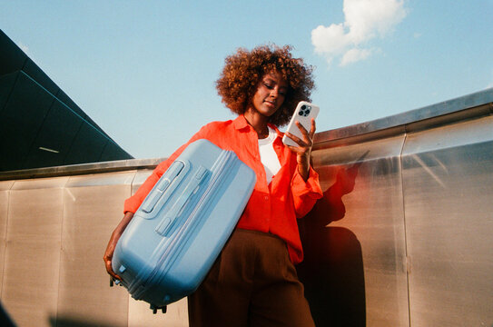 Woman checking smartphone with blue suitcase during travel