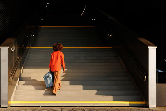Woman traveler pulls blue suitcase up transit station stairs