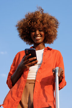 Woman checking smartphone with luggage under blue sky