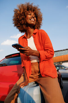 Woman holding smartphone beside suitcase and red car