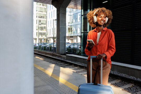 Woman with headphones holding smartphone at train platform