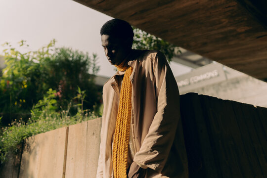 Moody portrait of young Black man beneath concrete overhang.