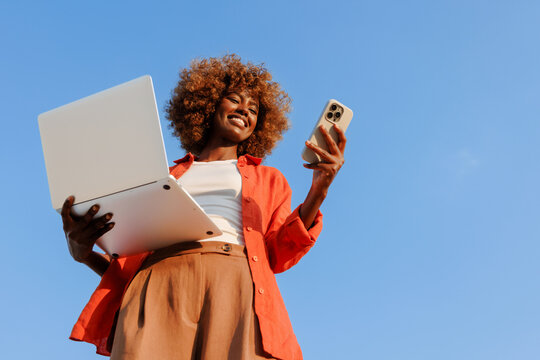 Woman using smartphone and laptop under blue sky