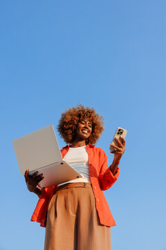 Woman holding laptop and smartphone under summer sky