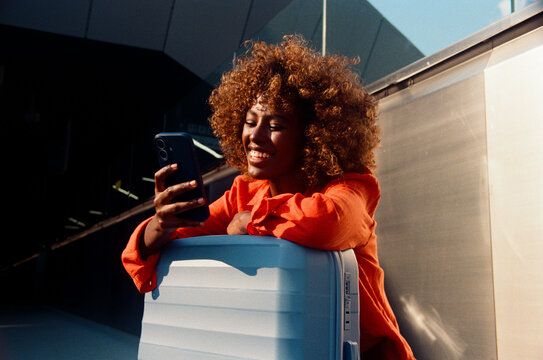 Woman checks smartphone beside blue suitcase