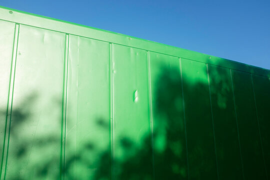 Green metal shipping container, sunlight and  shadow of tree