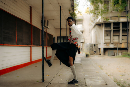 Young Black fashion model posing beside urban walkway.
