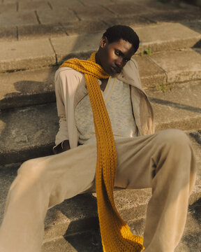 Young Black man sitting on concrete steps wearing knit scarf