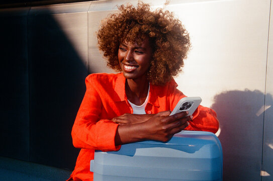 Woman holding smartphone beside blue suitcase during travel