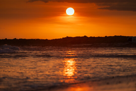 Vivid Orange Sunset Over Ocean with Rocky Silhouette