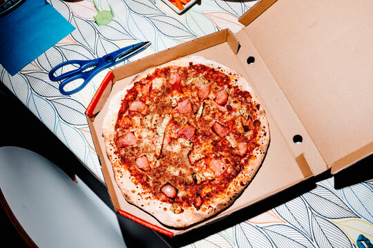 an open pizza box with blue kitchen scissors beside it
