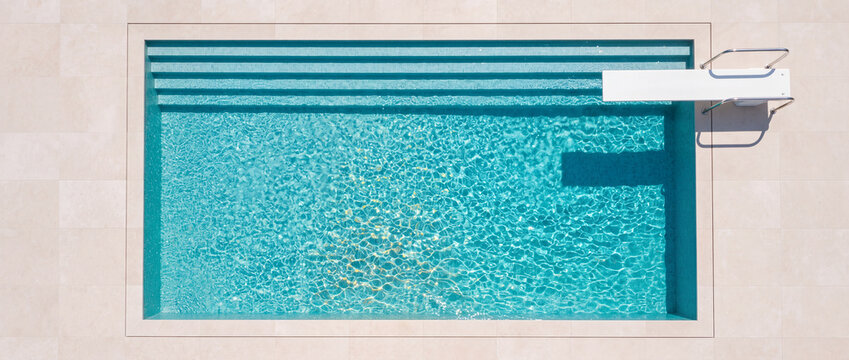 Swimming pool aerial view with turquoise water, clean beige stone deck, built-in steps, and white diving board, ideal for summer vacation, luxury resort, and travel leisure backgrounds