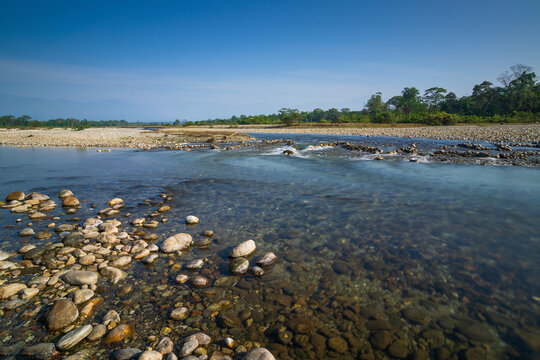 Murti river in the morning, riverbed in foreground with flowing water and stones. Scenic beauty of Dooars landscape, West Bengal, India. Dooars is popular tourist destination for natural landscapes.