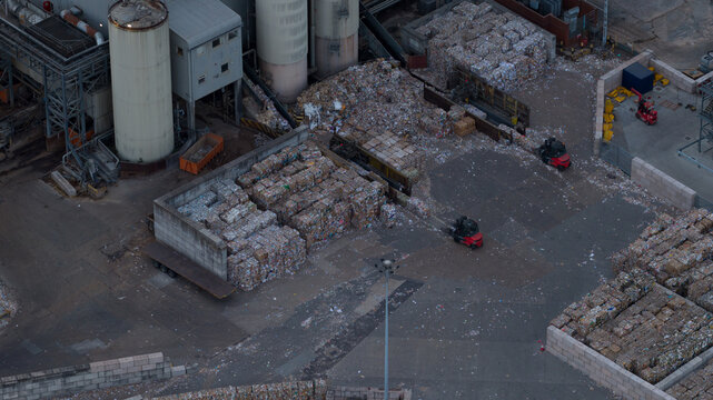 Aerial view of a recycling facility with large stacks of baled paper, industrial silos, and forklifts operating in the yard, Sittingbourne, England, United Kingdom.