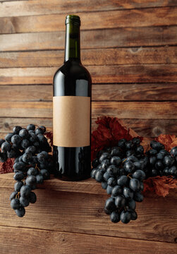 Red wine bottle with blue grapes on an old wooden table.