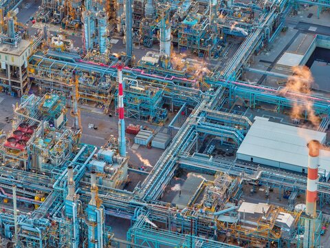 Aerial view of the industrial chemical plant in Bantzenheim, featuring complex networks of blue pipes, tall chimneys with smoke, and storage tanks in Bantzenheim, Grand Est, France.