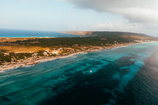 Aerial view of Formentera coastline with turquoise waters, sandy beaches, and lush greenery under a cloudy sky in Balearic Islands, Spain.