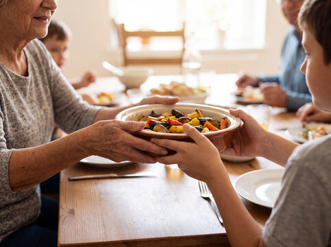 Grandmother passing bowl of roasted vegetables to grandson at table