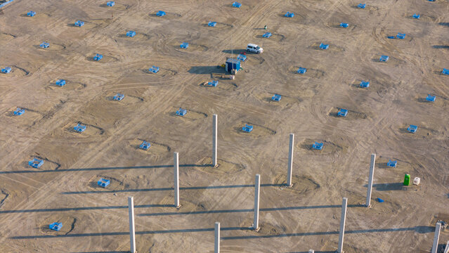 Aerial view of a logistics park construction site featuring concrete pillars, scattered blue markers, and tire tracks on the dirt ground in Fiorenzuola d'Arda, Emilia-Romagna, Italy.