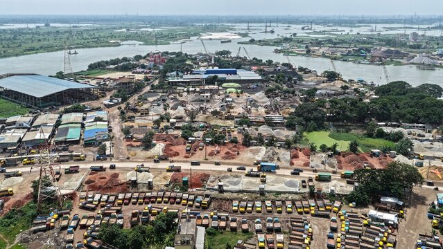 Aerial view of the Gabtoli area in Dhaka, featuring a large fleet of parked trucks, construction material stockpiles, industrial facilities, and the Turag River, Dhaka, Dhaka Division, Bangladesh.